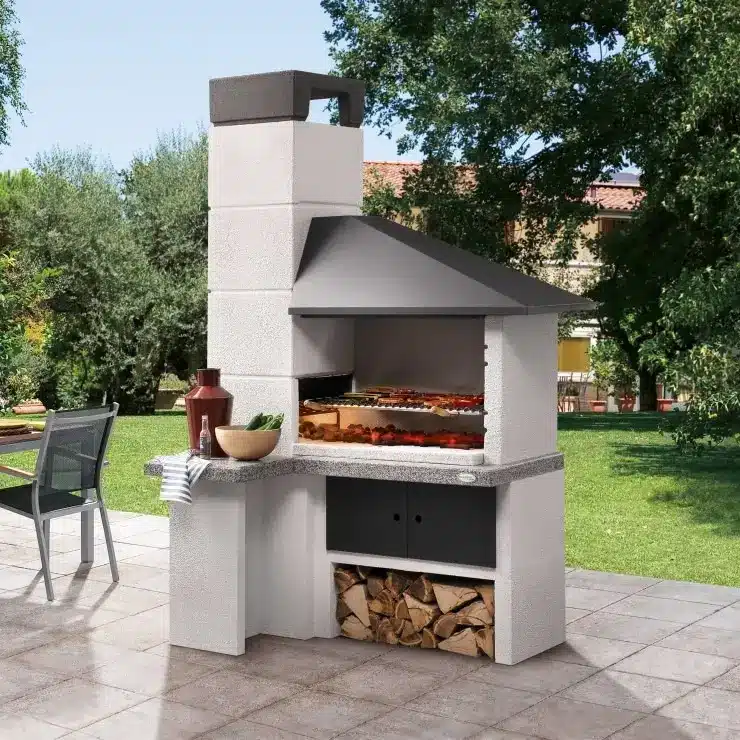 Barbecue in muratura e acciaio con piano di lavoro e legnaia in giardino